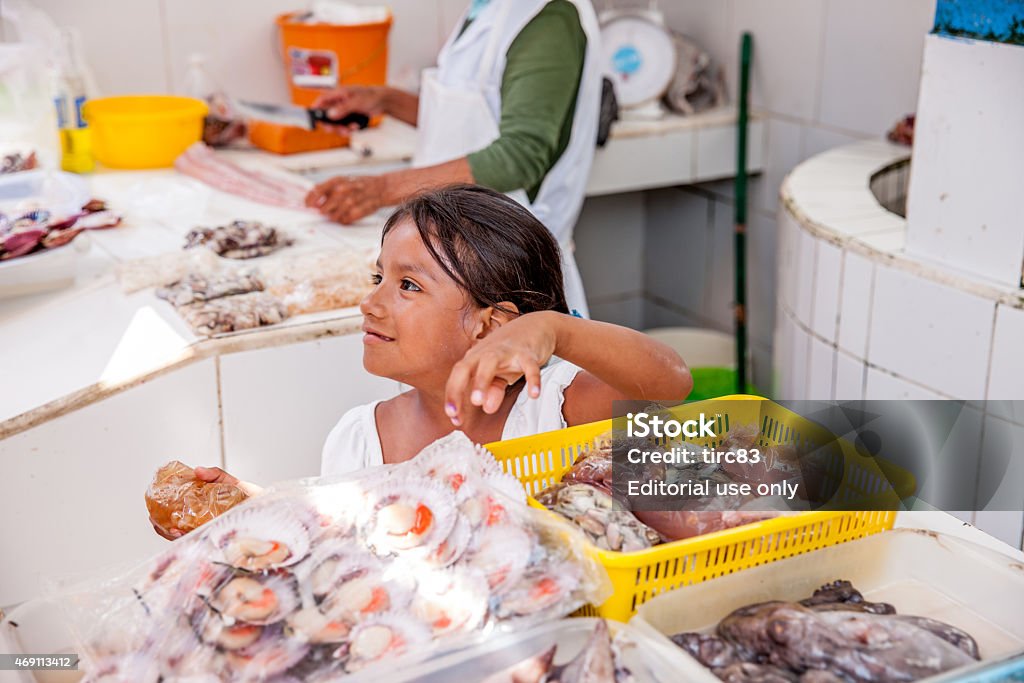 Hispanic girl helping her mother at the fishmongers Pucusana, Peru - January 12, 2015: Hispanic girl helping her mother serve raw fresh fish at the fishmongers in Pucusana, Peru Fish Stock Photo