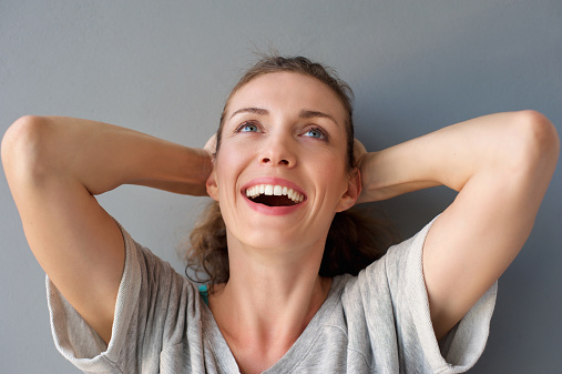 Close up portrait of a carefree happy woman laughing with hands in hair against gray background