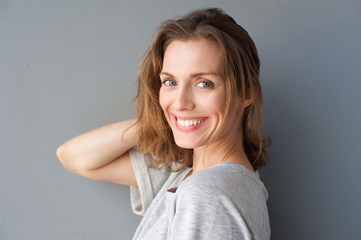 Close up portrait of a happy smiling beautiful woman posing with hand in hair against gray background