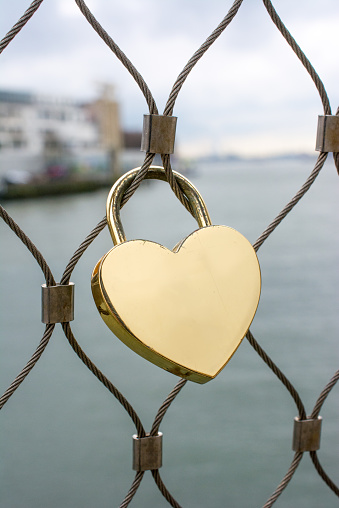 Love lock with carved heart hanging on the metal railing on the bridge. Green blurred background. Beautiful summer day.