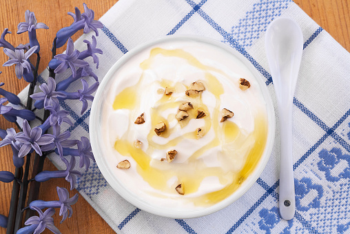 Creamy white Greek Yogurt with honey and nuts served on wooden table with cloth, spoon and purple Hyacinth for decoration.