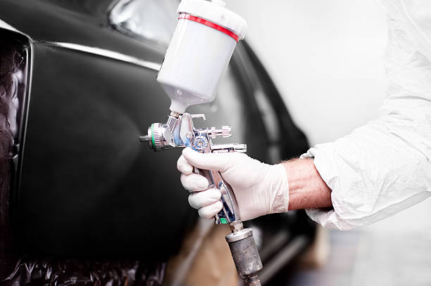 Worker using paint spray gun for painting a car Worker using paint spray gun for painting a car enamel wear stock pictures, royalty-free photos & images