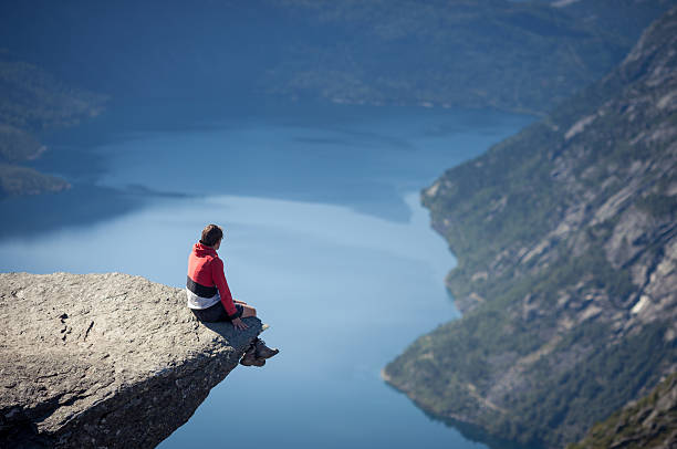 man sitting on trolltunga rock in norway stock photo