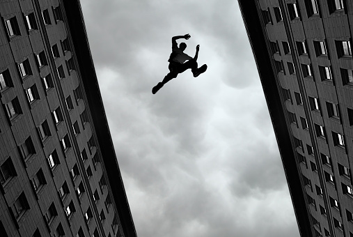 Man jumping over building roof against gray sky background