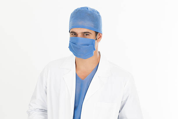 Portrait of confident female surgeon. Healthcare worker is wearing surgical mask. She is against illuminated lights in operating room at hospital.