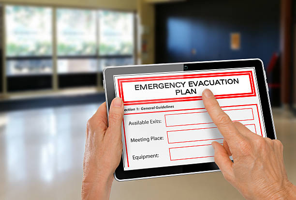 Hands with Computer Tablet and Emergency Evacuation Plan by Doors stock photo