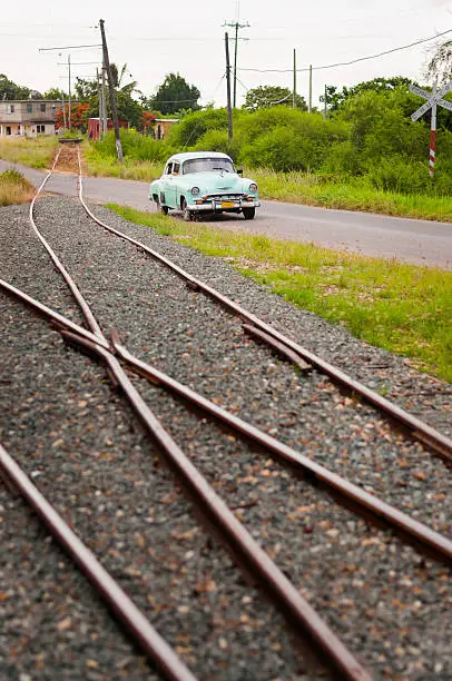An old turquoise car in a rural road near Havana alongside a train railroad.