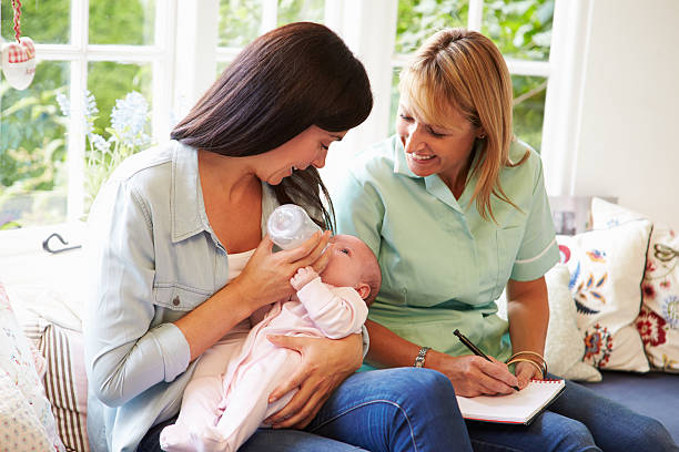 Mother bottle feeding a baby and meeting with health advisor Mother With Baby Meeting With Health Visitor At Home Midwife stock pictures, royalty-free photos & images