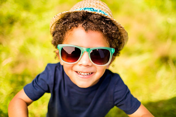 Little boy smiling at camera in park Small kid cheerfully smiling at camera with hat and sunglasses garden accessories stock pictures, royalty-free photos & images