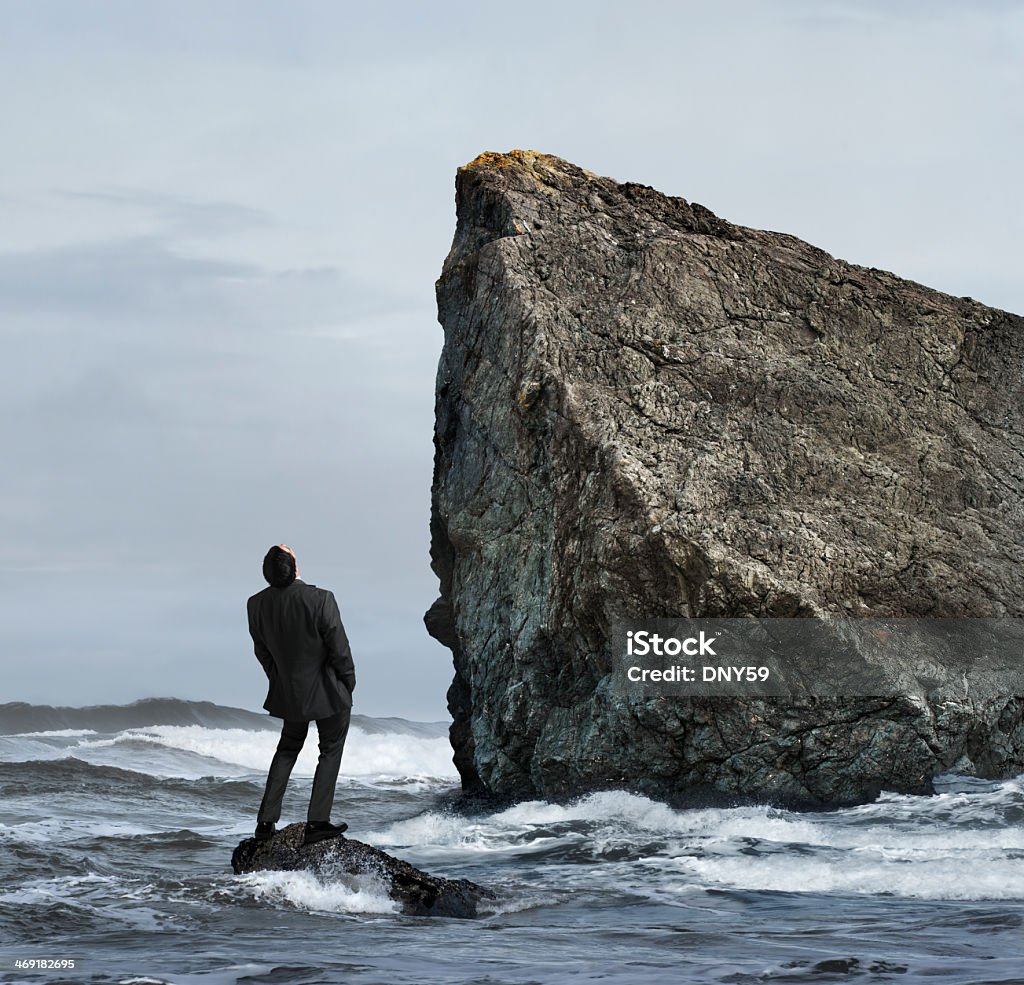 Adversity A businessman in the ocean looking up at cliff. Cliff Stock Photo