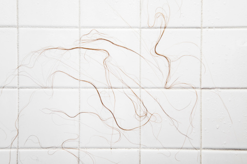 Close-up of long wet hair strands sticking to shower tiles as a result of chemotherapy.