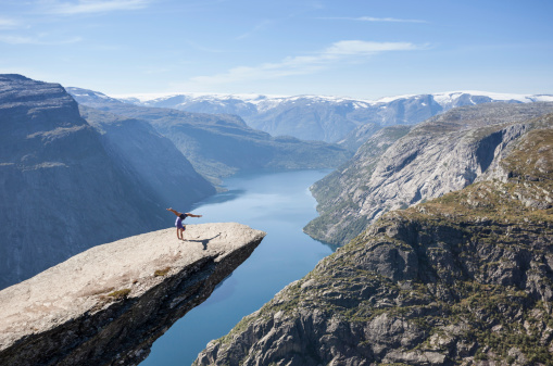 female gymnast doing a handstand on trolltunga rock above lake in norway