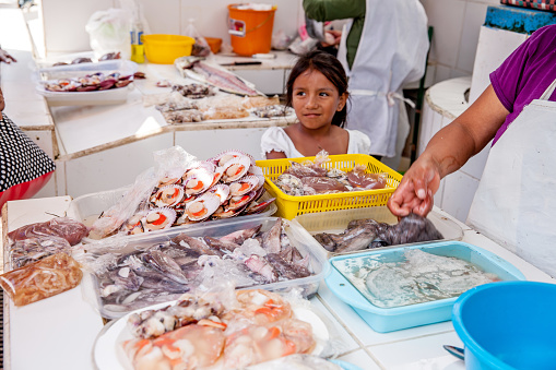 Pucusana, Peru - January 12, 2015: Hispanic girl helping her mother serve raw fresh fish at the fishmongers in Pucusana, Peru