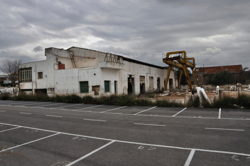 Abandoned factory exterior and empty parking lot under cloudy winter sky.