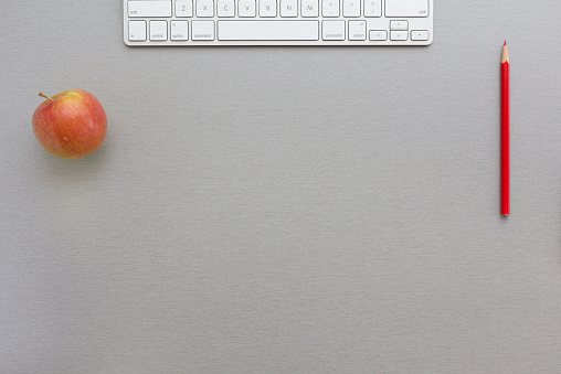 Creative office style composition with red apple, keyboard and red pencil located on grey wooden desk. Top view