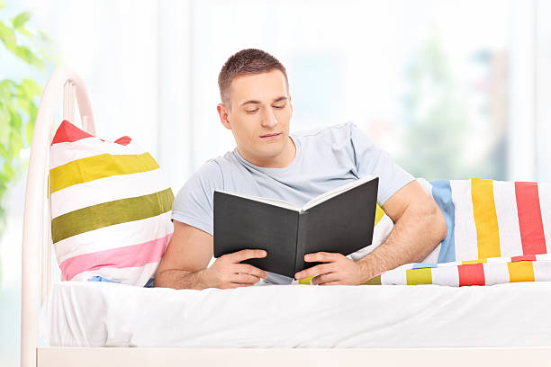 istock Relaxed young man reading a book in bed 469208138