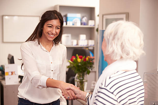 A female physician greeting an elderly woman in the office Receptionist Greeting Female Patient At Hearing Clinic, Smiling Shaking Hands receptionist stock pictures, royalty-free photos & images