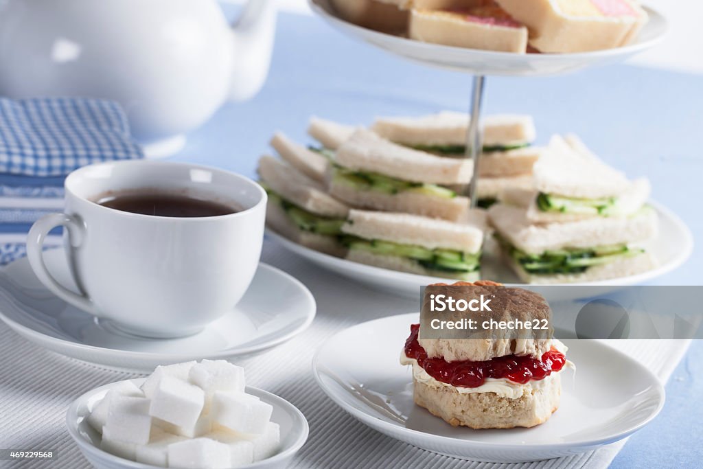English Tea Time Cup of tea with sugar cubes and scones, cucumber sandwiches in the background Afternoon Tea Stock Photo
