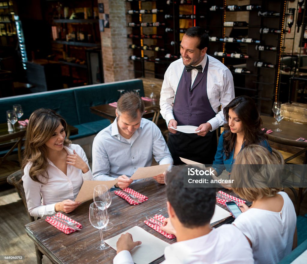 Friends having dinner at a restaurant Group of friends having dinner at a restaurant and waiter holding menu 2015 Stock Photo