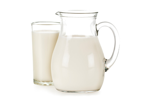 Side view of a glass pitcher filled with milk against white backdrop, the pitcher has a handle on the right side and on left side there is a glass full of milk. The image includes an excellent clipping path.