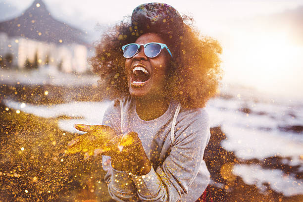 Afro hipster girl laughing ecstatically while throwing gold glitter Laughing Afro hipster girl having fun throwing gold glitter from her hands while at tthe beach at sunset hipster fashion stock pictures, royalty-free photos & images