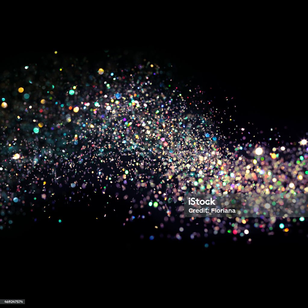 Flowing stars in all colors Light shimmers against a flow of multicolored and dense holographic glitter as it waving across an empty field. Out of focus at the front side of the image, the thousands of tiny metallic flakes spill downwards towards the background, where sharper focus defines the individual pieces. The motion of the sparkling glitter weaves and bends as it moves withe dense concentration from left to the right, and shines in all colors.  Empty black space frames the colored shimmer on the upper and lower portions of the picture. Studio shot using high speed technique.  Glowing Stock Photo