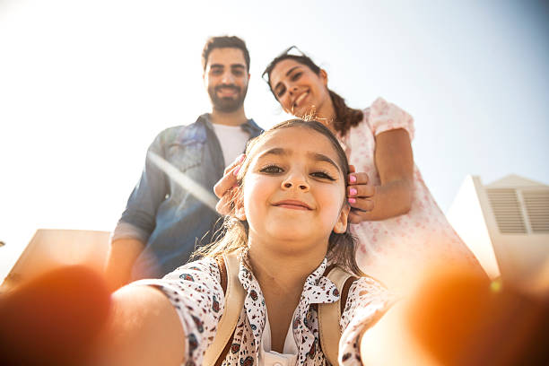 Girl taking a selfie with parents Little girl enjoying the weekend outdoor during a sunny day. She's holding the phone and taking a selfie to her and her parents. arabian girl stock pictures, royalty-free photos & images