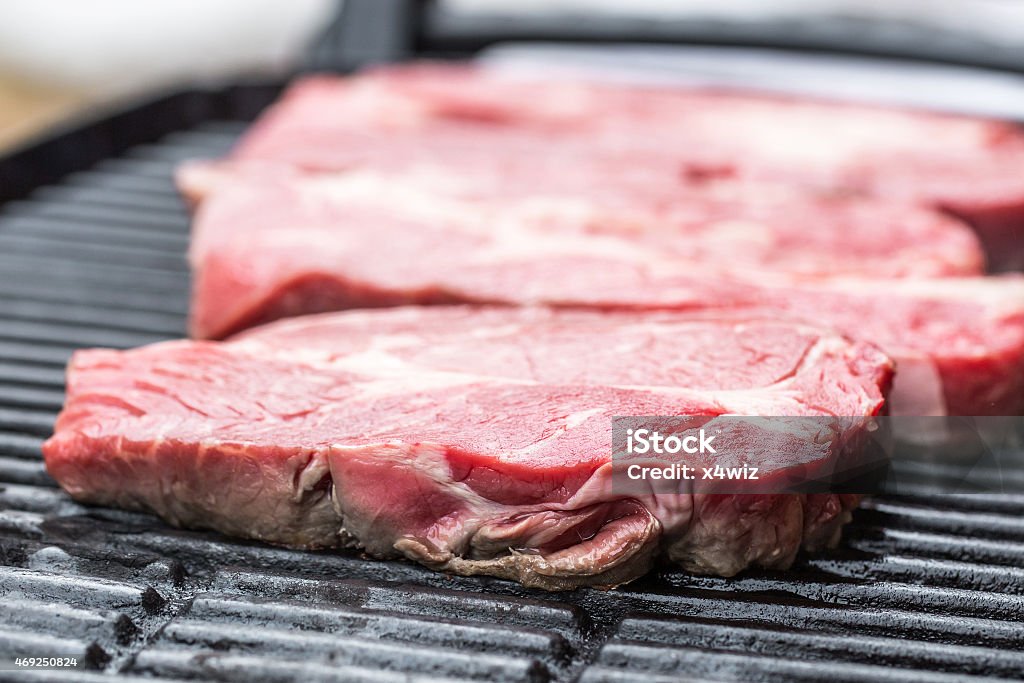 Fresh beef steaks on grill or BBQ Raw fresh beef steaks being fryed or prepared on grill or BBQ 2015 Stock Photo