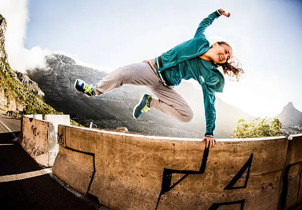 A breakdancing teen jumping over a wall parkour style