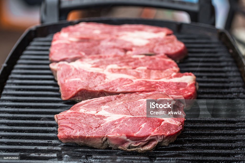 Fresh beef steaks on grill or BBQ Raw fresh beef steaks being fryed or prepared on grill or BBQ 2015 Stock Photo