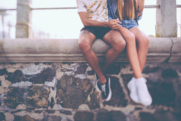 Legs of hipster couple sitting on a wall holding hands Cropped image of the legs of a hipster couple holding hands and sitting on a wall made of rough textured stone teen romance stock pictures, royalty-free photos & images