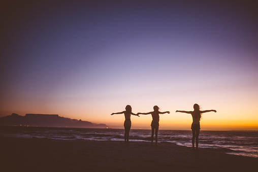 Silhouette of friends at the sea with arms outstretched at twilight