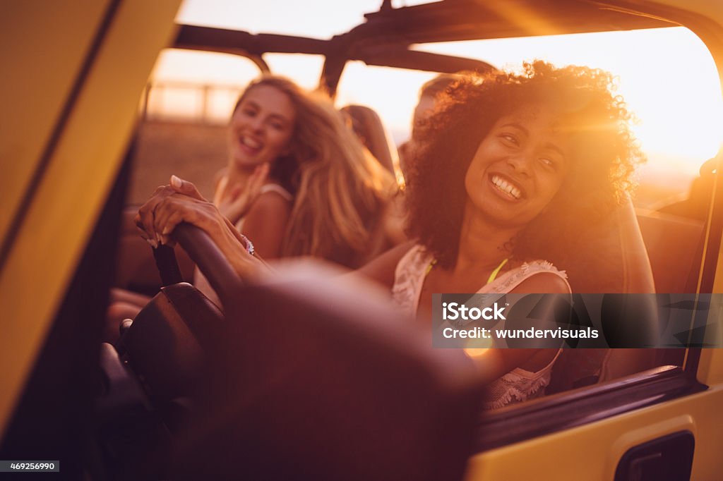 Afro girl with friends on a road trip at sunset Smiling Afro girl with girl friends on a summer vacation road trip at sunset Car Stock Photo