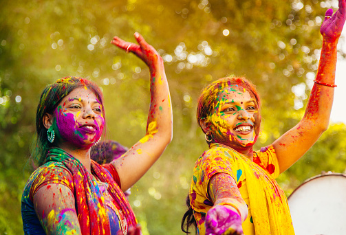 Two young Indian women, with their colorful faces and clothes, dancing to the beat of daffali (Indian tambourine) during the Holi Festival in Jaipur India.
