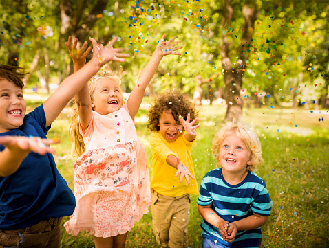 Friendly children happily having fun with colourful confetti in sunny park