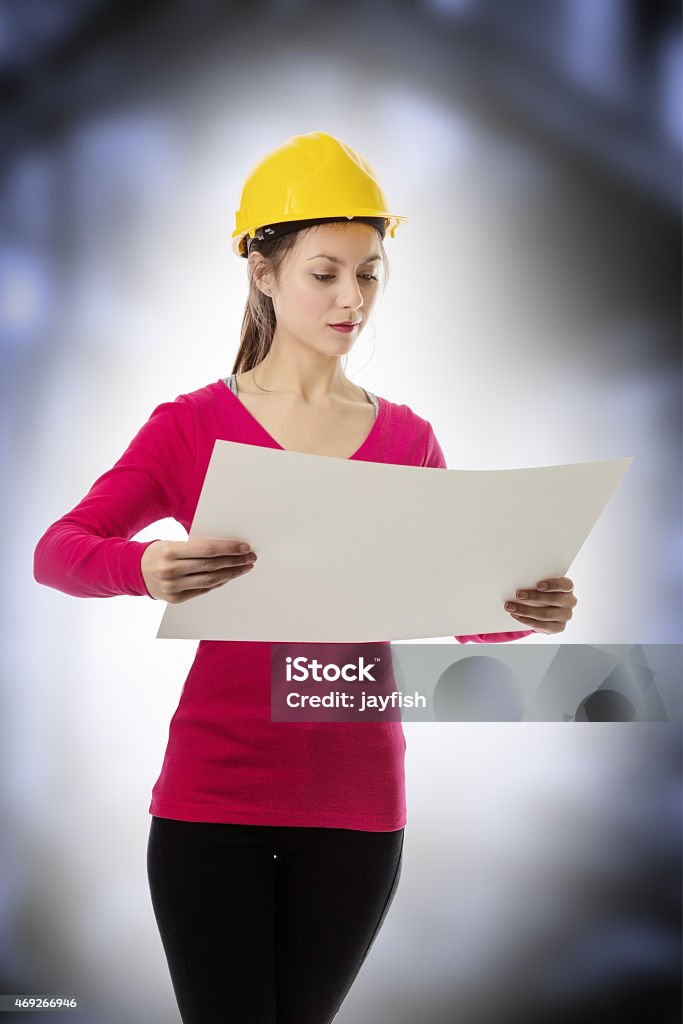 building plans woman looking at a large sheet of paper wearing a hard hat 2015 Stock Photo