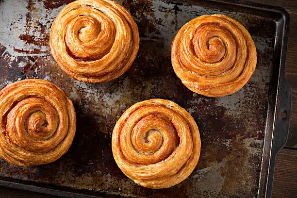 An extreme close up overhead horizontal photograph of several freshly baked cinnamon butter rolls on a well used, grungy old metal tray.