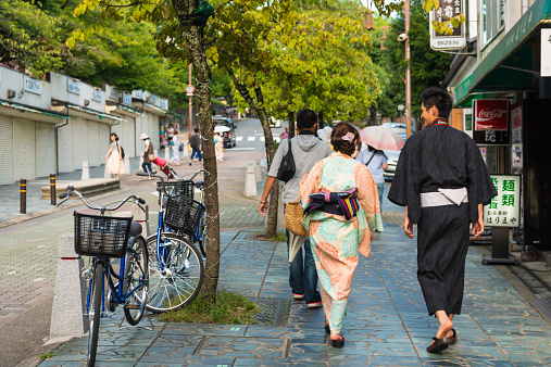 Nara, Japan - August 11, 2014: View of local residental street, a Japanese couple, man and woman dressed in traditional yukata walking down the street on pavement. Rear view. Few other people in distance walking on the other side of the street. 