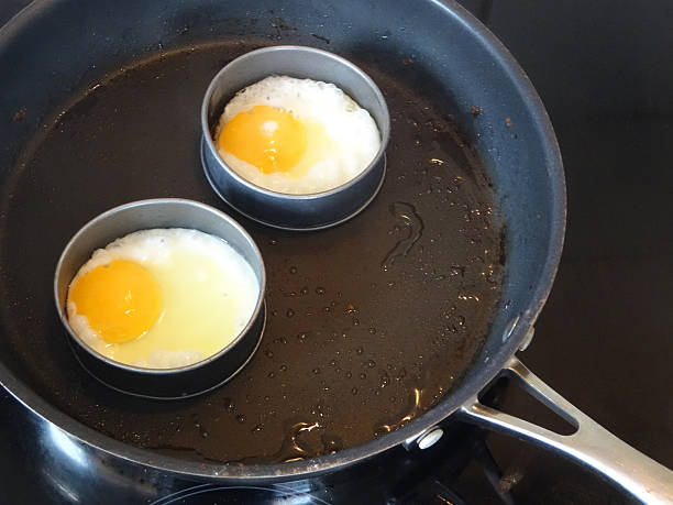 Image of fried eggs being cooking in frying-pan, non-stick rings Photo showing two fried eggs that are being cooked in a stainless steel, non-stick frying pan, on a ceramic hob.  These fried eggs are shaped in round, non-stick metal ring moulds, with the rings helping to contain the whites and yolks, stopping them spreading in the pan. metal molding stock pictures, royalty-free photos & images