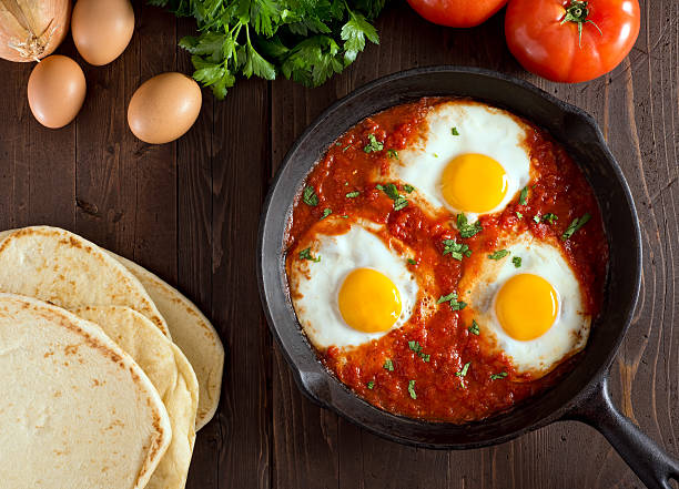 Upper view of dish of eggs poached in tomato sauce and cumin Shakshuka with eggs, tomato, and parsley in a cast iron pan. libyan culture stock pictures, royalty-free photos & images