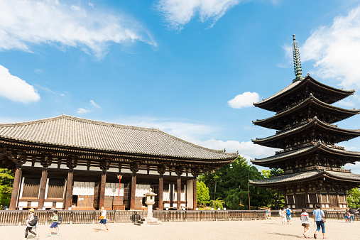 Nara, Japan - August 11, 2014: People walking in front of a wooden temple and pagoda on sunny summer day. Sky is blue with few white clouds. 