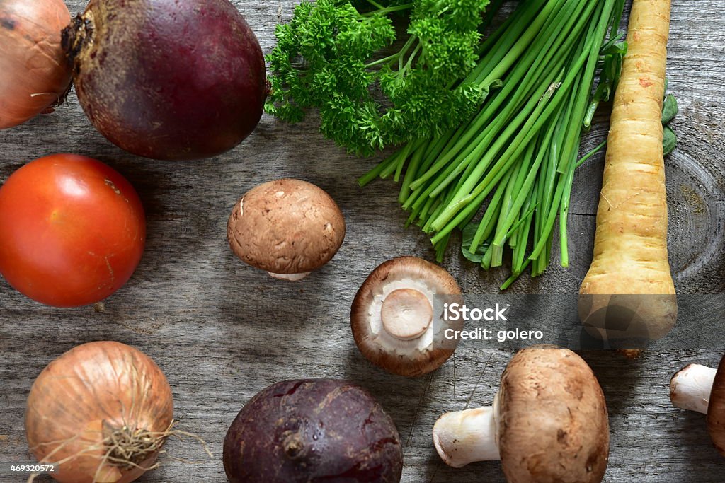 raw vegetables on wooden plank in the kitchen high angle view on still of regional food arranged on wooden plank , high angle view on parsley,chives, beetroot, mushrooms, onion and parsley root 2015 Stock Photo