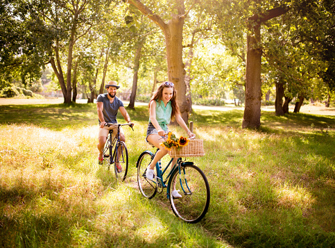 Happy young couple cycling in summer together  in a park