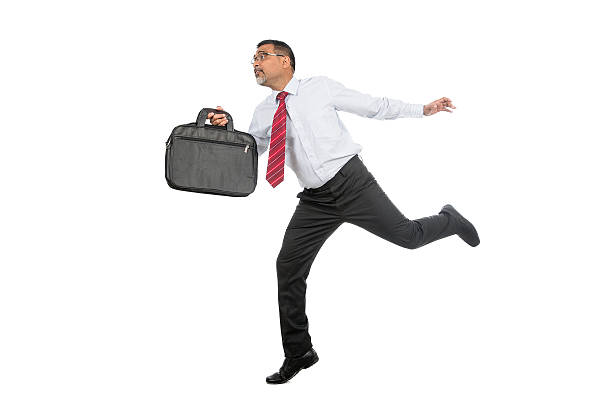 Full length image of a Mid Age businessman in formal clothing, running with his briefcase in his hand. Image isolated on white background. He is in black trousers, white shirt and red tie. He is holding the briefcase in one hand and the other hand is stretched out.