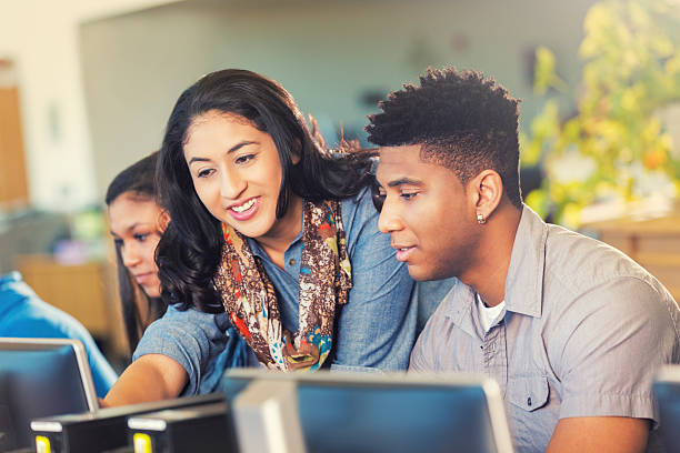 Hispanic teacher helping an African American teen with work. Production Tool Ref #12 computer lab stock pictures, royalty-free photos & images