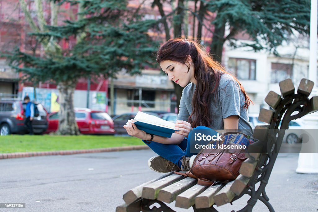 Beautiful young happiness girl sitting on bench and reading book. Student sitting on old wood bench and reading blue book in the park. 2015 Stock Photo