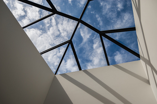 Looking up at the ceiling of a home through a large and elegant skylight. Interesting lines and shadows play together to create a dynamic composition that capture the stye of modern architecture and interior design.