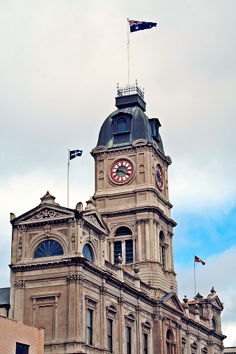 Perspective portrait shot of the old Town Hall buildings in Ballarat with the Australian, Aboriginal and Eureka 'Southern Cross' flags flying proudly against a dramatic sky.