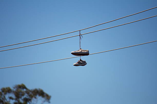 A low angle view of a pair of white sneakers hanging from their shoelaces on a power line against the teal blue sky.