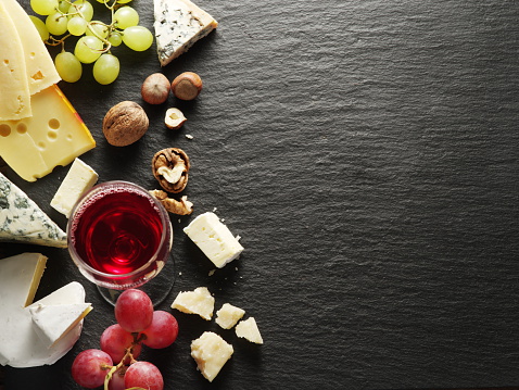 Different types of cheeses with wine glass and fruits. Top view.